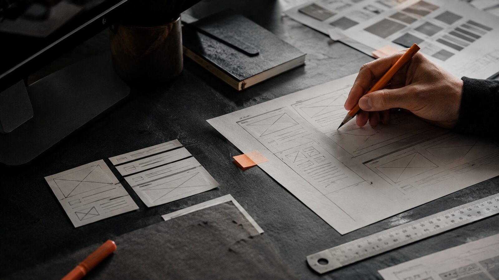 Hands sketching website wireframes on a dark worktable